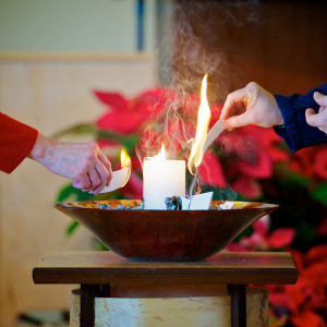 Image of two hands lighting candles seated in a decorative bowl